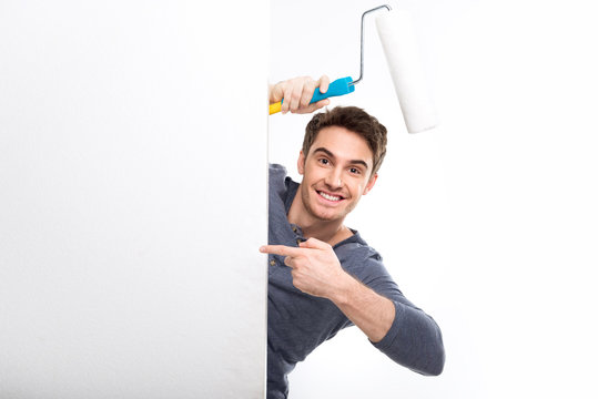 handsome man holding paint roller and pointing on blank card isolated on white, handyman tools concept