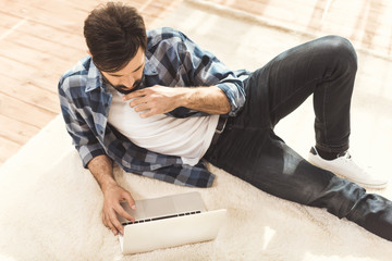 man lying on carpet and using laptop