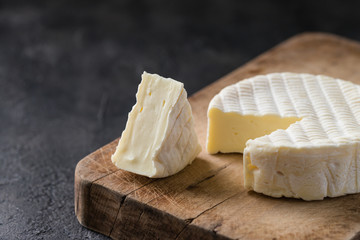 French soft cheese from Normandy region with a slice on a wooden board on dark rustic background