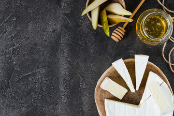 Soft cheese brie sliced on wooden cut with honey and pear on dark rustic background with copy space, top view
