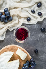 French soft cheese from Normandy region sliced on a wooden cut with red grapes and glass of red wine on dark rustic table, blurred background, top view