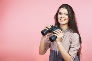 Young woman with binocular glasses on pink background