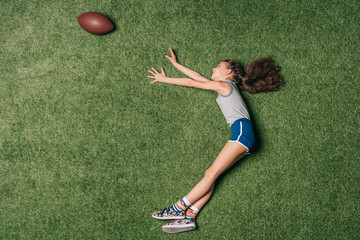 top view of little sportive girl catching rugby ball on grass, athletics children concept