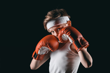 boy obscuring face with boxing gloves isolated on black, active kids concept