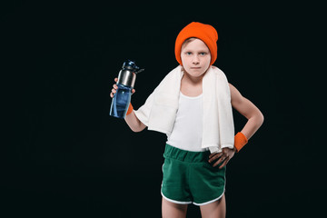 Confident sporty boy with towel on neck holding sports bottle with water isolated on black