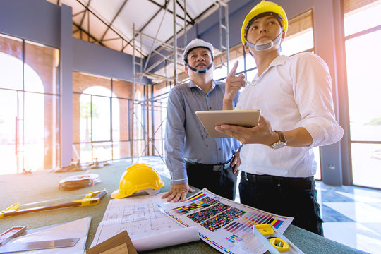 customer and constructor foreman worker with helmet and vest looking blueprints in new house building in real state business and housing industry concept. data in touch pad