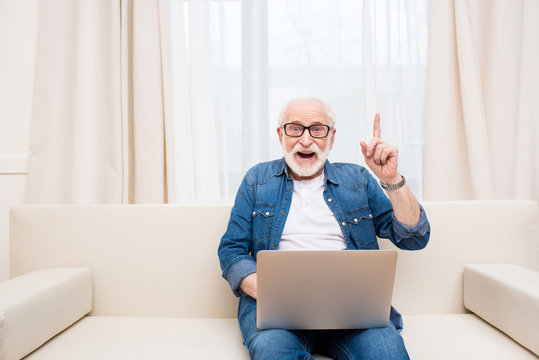 Smiling senior man using laptop and pointing up with finger