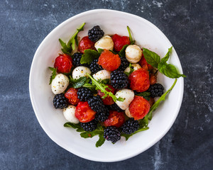 Delicious fruit salad with mozzarella in white plate on dark background.