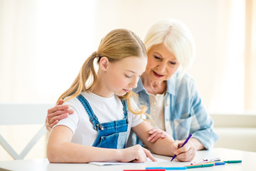 Smiling senior woman and preteen girl drawing together at table