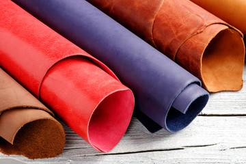 Brightly colored leather in rolls on the white wooden background. Leather craft.