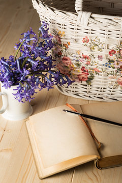 aged notebook with brush and lily flowers in a white cup and white basket - copy space