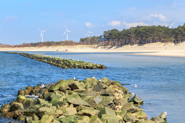 Darłówek, plaża na wybrzeżu Bałtyku. Widok infrastruktury chroniącej przed falami i służącej wypoczywającym tu ludziom 