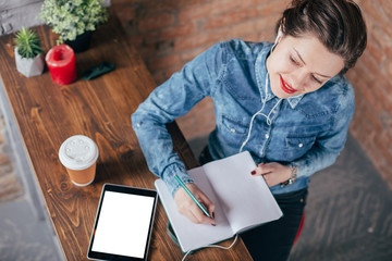 Beautiful young female freelancer with notepad and tablet have a coffee break in loft interior room