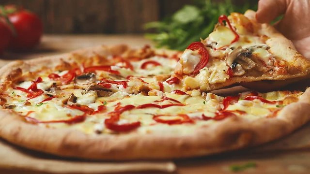 Close-up of fresh cooked Italian pizza on wooden table. Female hand taking pizza slice.  