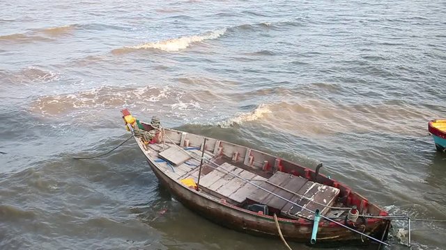 Fisherman's boat on dirty beach, full of different stuff. Wind is blowing and sandy, rocky beach in Monsoon season of thailand