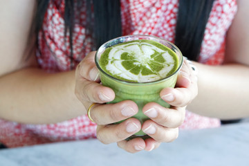 A Woman's hand holding a cup of Matcha green tea with latte art, The traditional Chinese and Japanese Tea. 