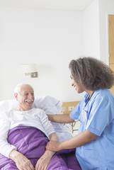 Reassuring confident african female doctor visiting elderly caucasian patient in hospital bed