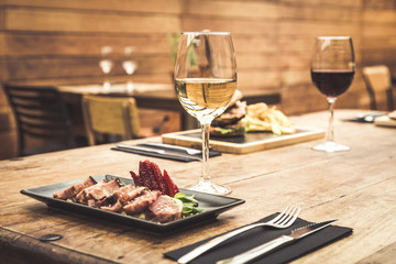 Traditional restaurant atmosphere with tuna tataki and burger with chips in the background on rustic wooden table and glass of white wine