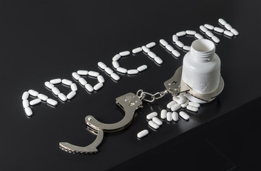 Get addicted to drugs or free from addiction to medicine. Drug and narcotics abuse or after rehab concept. Addiction written with pills. Medicine spilling out from a bottle locked with open handcuffs.