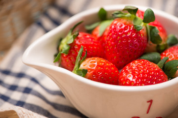 Bowl with fresh strawberry on blue wooden table.