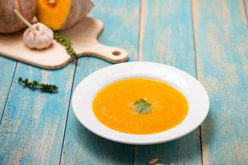  Top view of pumpkin and carrot soup with cream and parsley on blue  wooden background.
