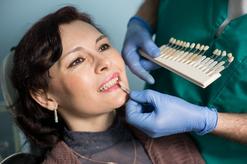 Close-up portrait of woman in dental clinic office. Dentist checking and selecting colour of the teeth, making the process of treatment. Dentistry