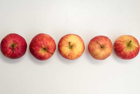 High Angle View Of Five  Red Gala Apples Arranged In A Row On A White Table (selective Focus)