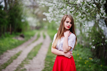 Portrait of beautiful girl with red lips at spring blossom garden, wear on red dress and white blouse.