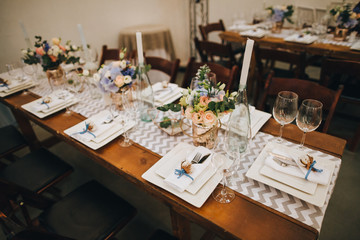 The wooden festive table is decorated with compositions of flowers, candles and served with cutlery, glasses and plates