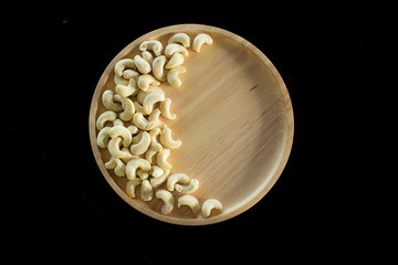 Cashew nuts in wooden plate isolated on black background