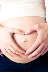 A pregnant woman touches her naked stomach, showing her hands a heart shape around the navel
