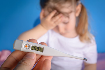 Sick little girl holds her head with 38 degrees centigrade body temperature on a digital thermometer