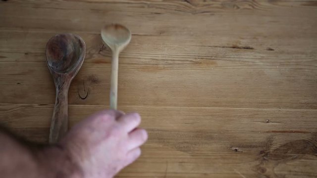 closeup of hand putting several wooden spoons on wooden table
