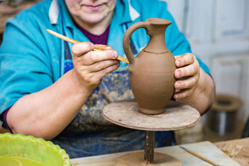 Fototapeta na wymiar An elderly woman decorates a clay pitcher on a potter's wheel 