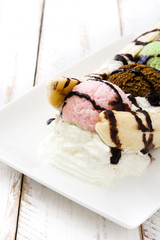 Banana split ice cream dessert with chocolate syrup on white wooden table
