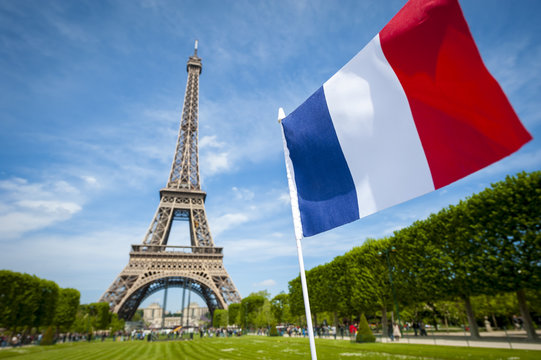 French tricolor flag flying in blue sky in front of the Eiffel Tower in Paris, France 