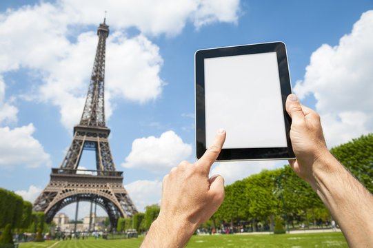 Hands holding a blank tablet in front of a bright view of the Eiffel Tower in Paris, France