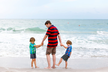 Two little kids boys and father on the beach of ocean