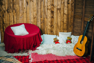 Obraz na płótnie Canvas Wooden wall, guitar and chair with pillows