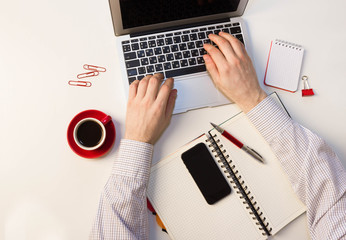 A man writes a pen in a notebook, to work in the office, laptop on a white table, a red mug of coffee.