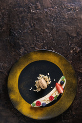 Food plating dessert organic banana with fresh berries, mint, puffed rice and macaroon biscuit served with turmeric powder on black plate over brown texture background. Flat lay, space