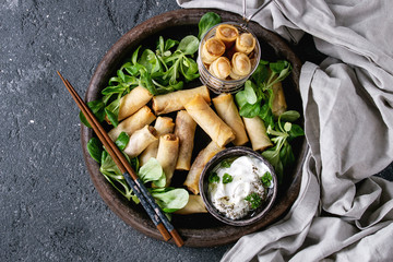 Fried spring rolls with white yogurt sauces, served in terracotta plate and fry basket with fresh...