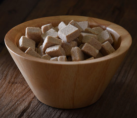 Brown sugar cubes in wood bowl on wood background