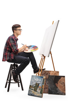 Teenage painter with paintbrush and palette looking at canvas
