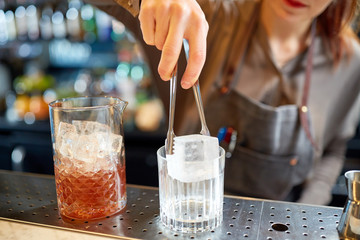 bartender adding ice cube into glass at bar