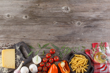 Ingredients for Italian dish. Parmesan cheese, pasta and fresh vegetables. On an old wooden background.