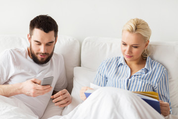 couple with book and smartphones in bed at home