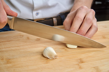Man's hands cutting fresh garlic in the kitchen, preparing a meal for lunch.