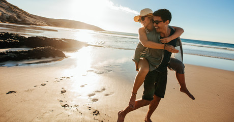 Man giving piggyback ride to girlfriend on beach