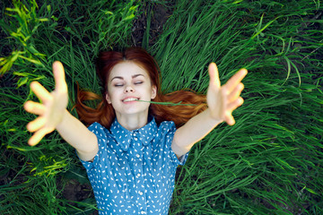 a woman with red hair extends her arms, grass